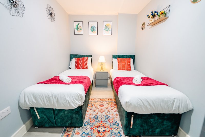 Twin bedroom with two beds, white pillows, red throws, botanical wall art and pendant lighting