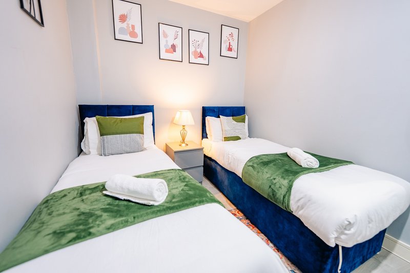 Bright twin bedroom with two single beds, navy headboards, green throws, white pillows and framed wall art