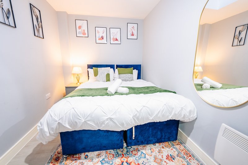Bright bedroom with blue upholstered bed, white bedding, green throw, framed wall art, and round mirror