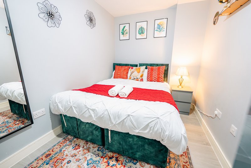 Bedroom with double bed, red and white bedding, teal headboard, wall art and mirror