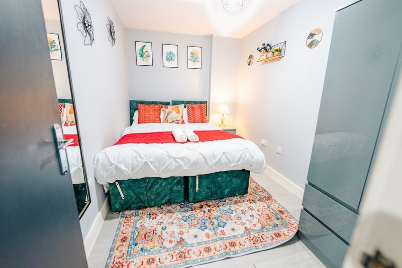 Compact bedroom with double bed, red bedding, patterned rug and wall art