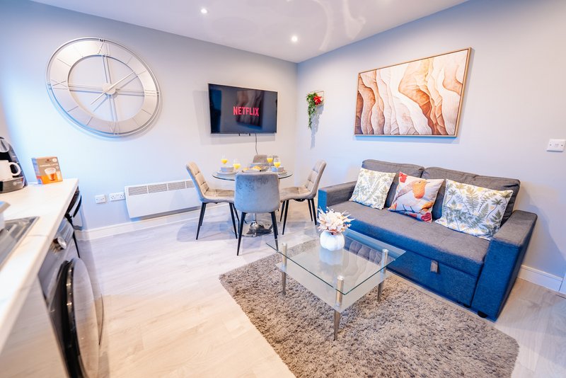 Modern open-plan living room with blue sofa, dining table, wall art, and TV mounted on wall
