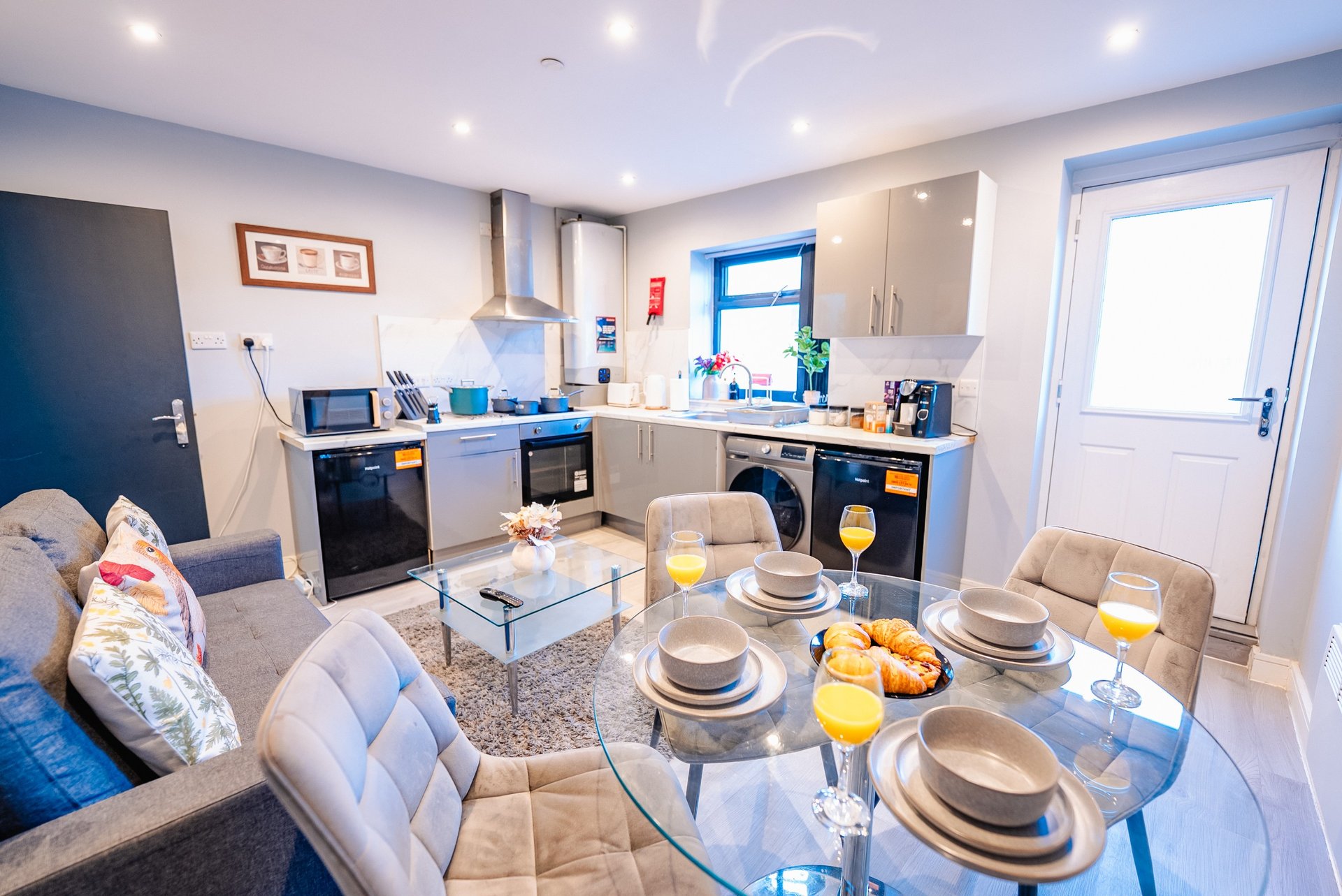 Open-plan kitchen-diner with grey cabinetry, dining table set for four, and lounge seating