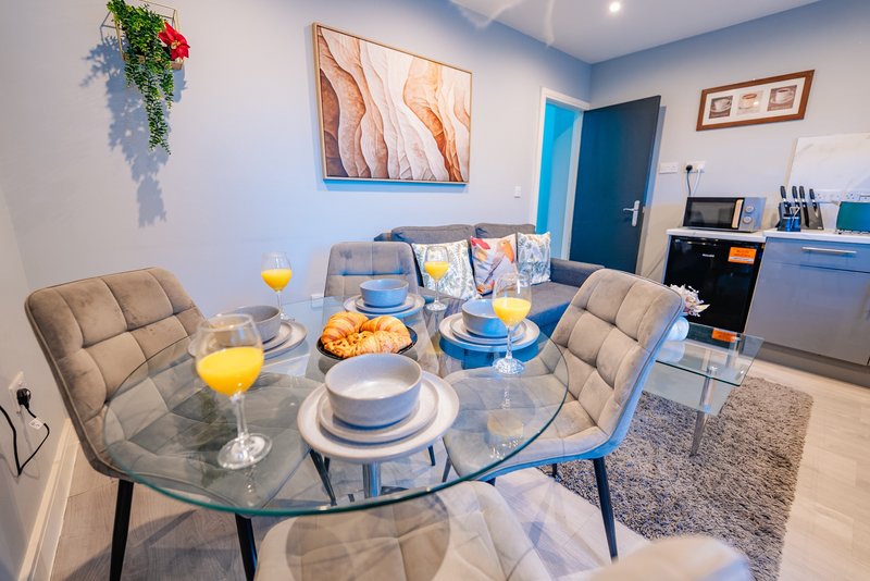 Modern dining area with round glass table, place settings, and kitchen visible in background