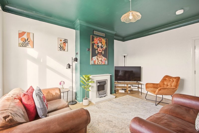 Modern living room with teal ceiling, leather seating, fireplace, TV, and colorful wall art