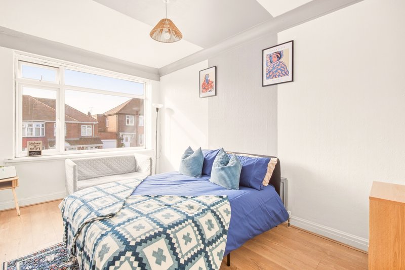 Bright bedroom with double bed, blue bedding, wooden floor and large window overlooking street