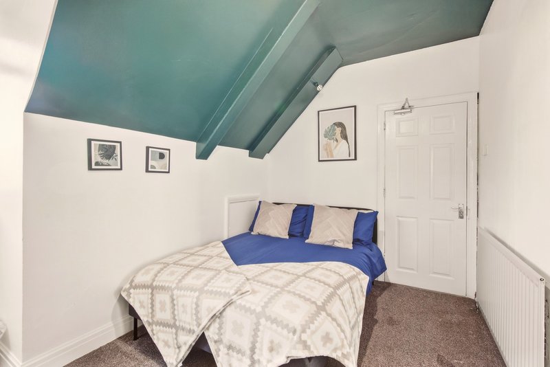 Attic bedroom with double bed, blue pillows, sloped ceiling and framed wall art