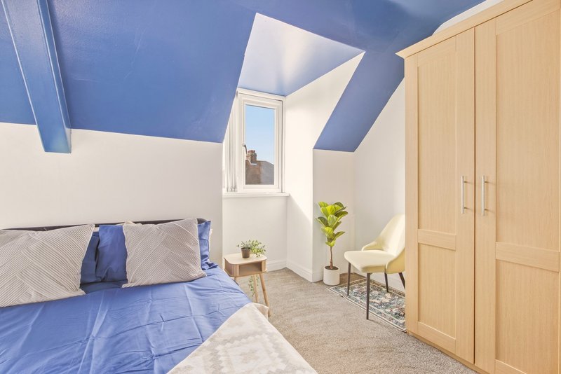 Modern bedroom with blue ceiling, double bed, wooden wardrobe and small seating area