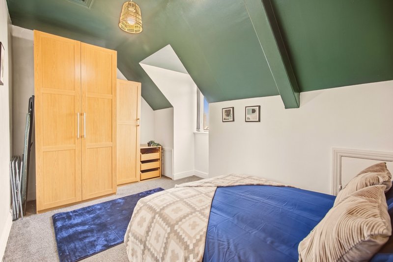 Attic bedroom with wooden wardrobe, blue bedding, angled ceiling and pendant light