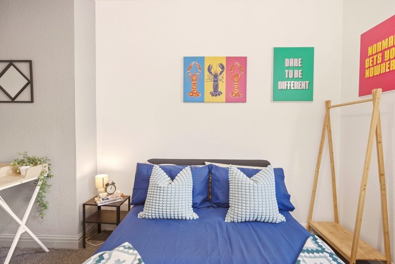 Bedroom with blue double bed, wooden frame, colorful wall art, and minimalist decor