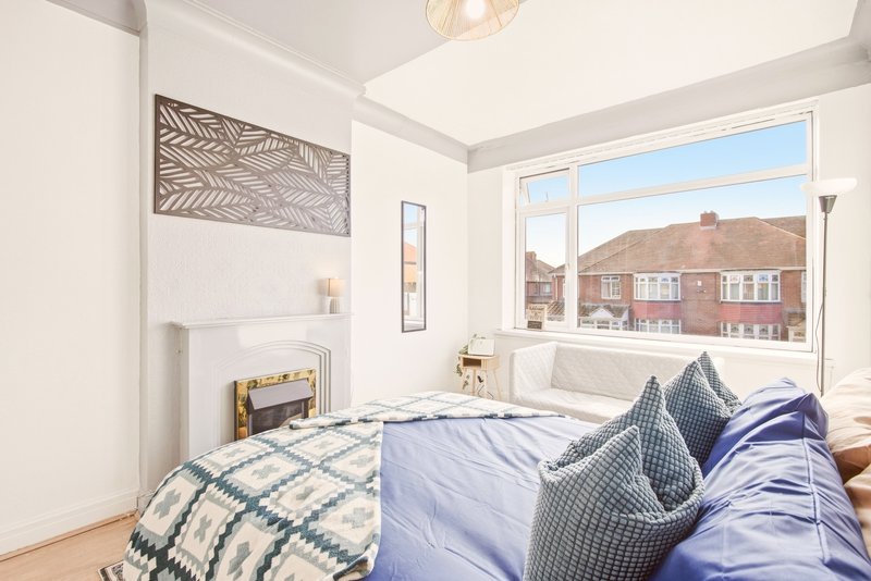 Bright bedroom with double bed, blue bedding, patterned cushions and large window overlooking street