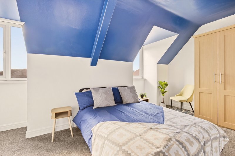 Modern attic bedroom with two beds, blue ceiling, wooden furniture and skylight window