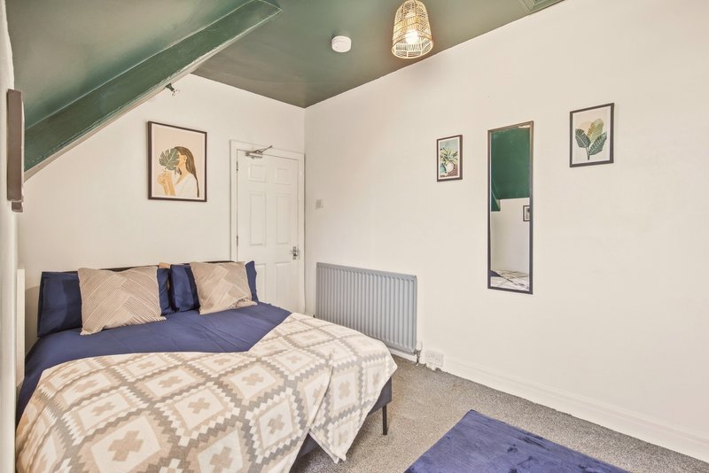 Bedroom with double bed, blue bedding, wall art, radiator and sloped ceiling