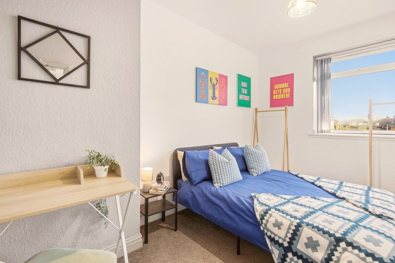 Bright bedroom with blue bed, wooden desk, wall art, and window with city view