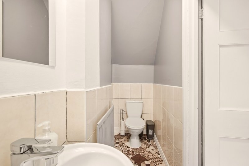 Bathroom with cream tile walls, white sink, toilet, radiator and patterned floor