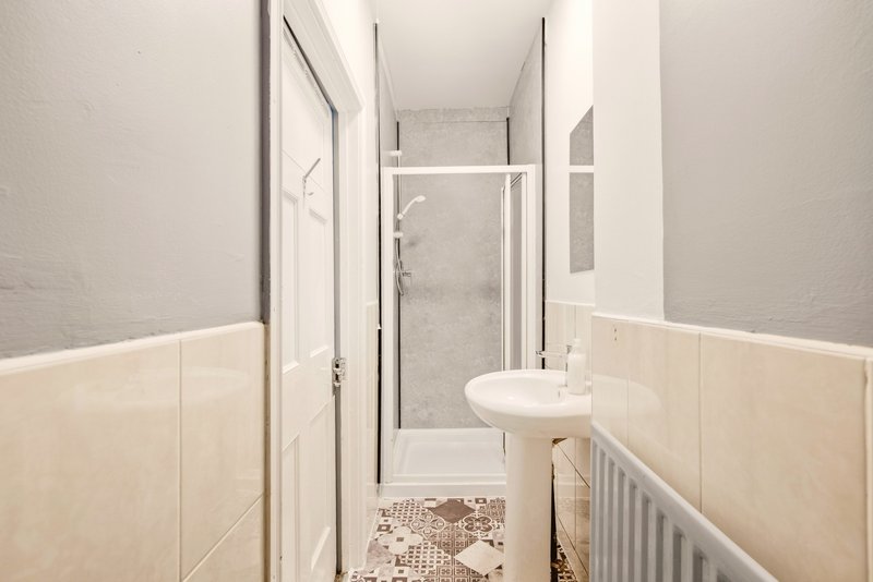 Narrow bathroom with shower cubicle, small sink, cream tile walls and patterned floor