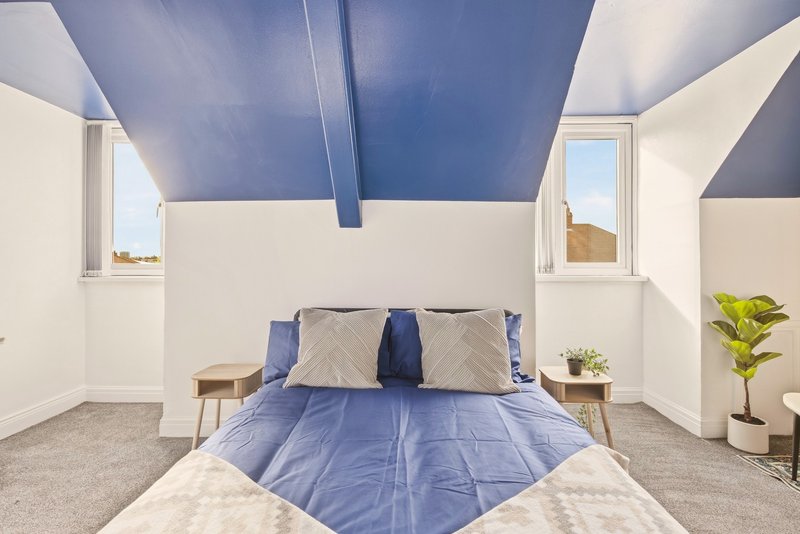 Bright modern bedroom with blue ceiling, double bed, cream bedding, and potted plant