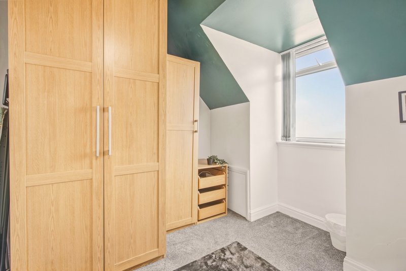 Attic bedroom with wooden wardrobe, skylight window, and grey carpet flooring