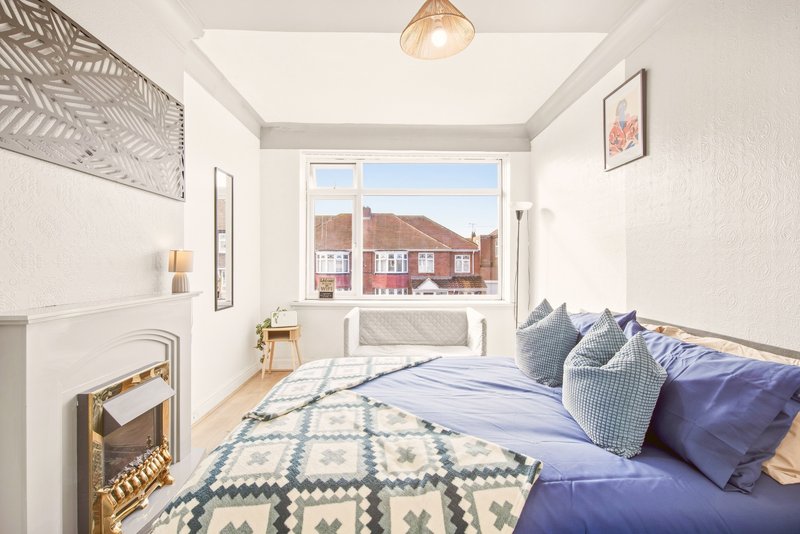 Bright bedroom with double bed, blue bedding, decorative pillows, fireplace and window with street view