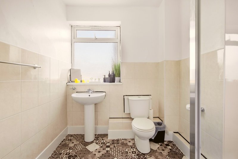 Bathroom with pedestal sink, toilet, window, and patterned floor tiles