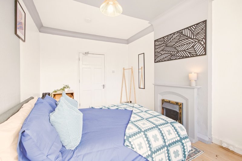 Bright bedroom with double bed, blue bedding, white walls, fireplace and pendant light