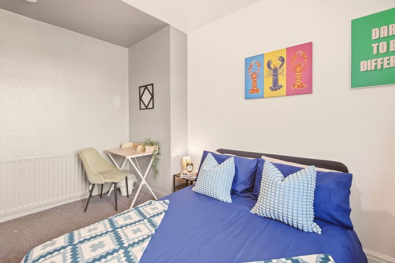 Bright bedroom with blue bed, white pillows, desk, chair and colorful wall art