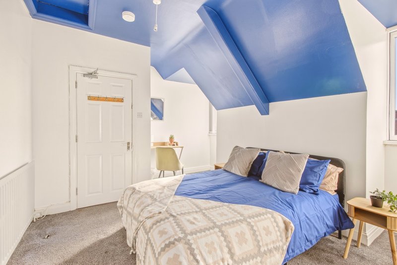 Bright bedroom with blue skylight, double bed, wooden nightstand and white door