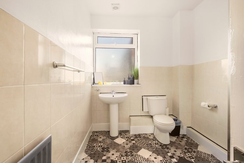Bathroom with pedestal sink, toilet, tiled walls, patterned floor and window