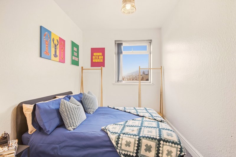 Small bedroom with blue bedding, colorful wall art, wooden frame and window view