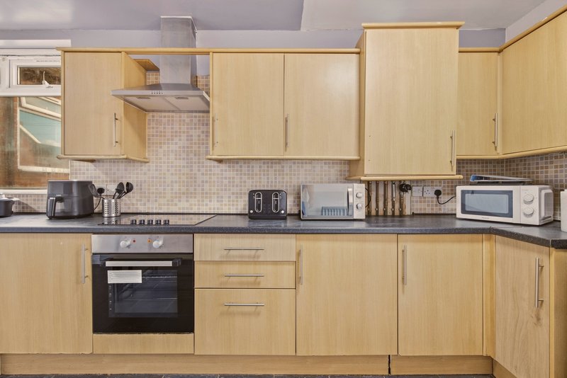 Modern kitchen with light wood cabinets, black countertop, built-in oven and gas hob