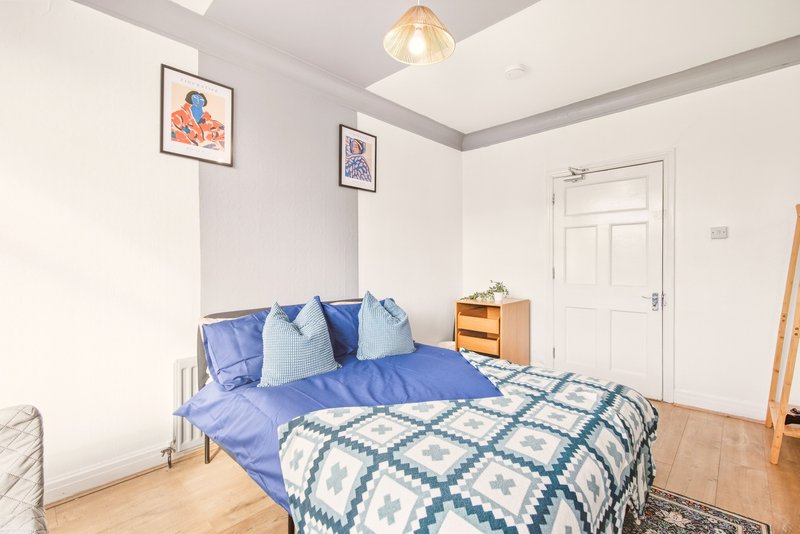 Bright bedroom with blue bedding, wooden bed frame, side table, and framed wall art