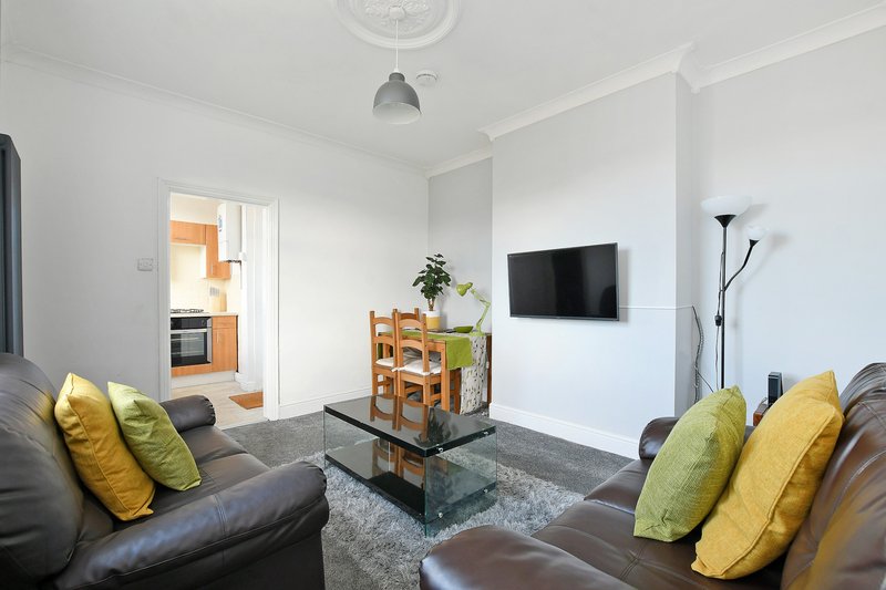 Modern living room with grey leather sofa, yellow cushions, wall-mounted TV and open-plan kitchen