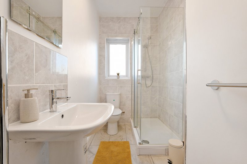 Modern bathroom with curved sink, shower enclosure, yellow bath mat and small window