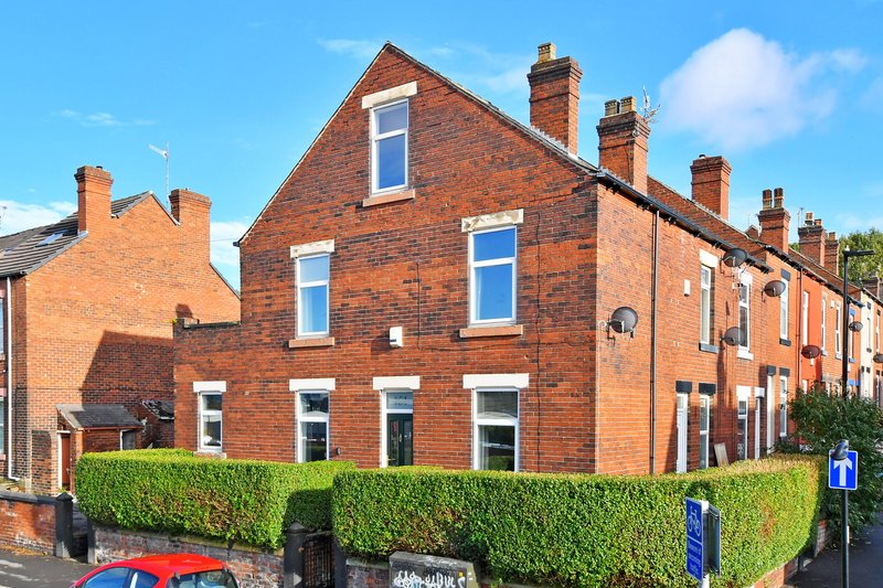 Red brick Victorian terraced house with blue windows, green hedge, and street view