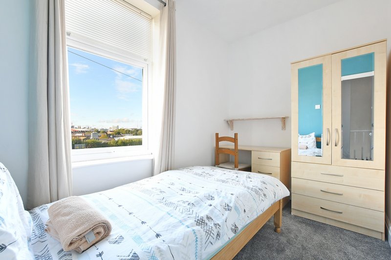 Bright bedroom with single bed, wooden furniture, window with city view