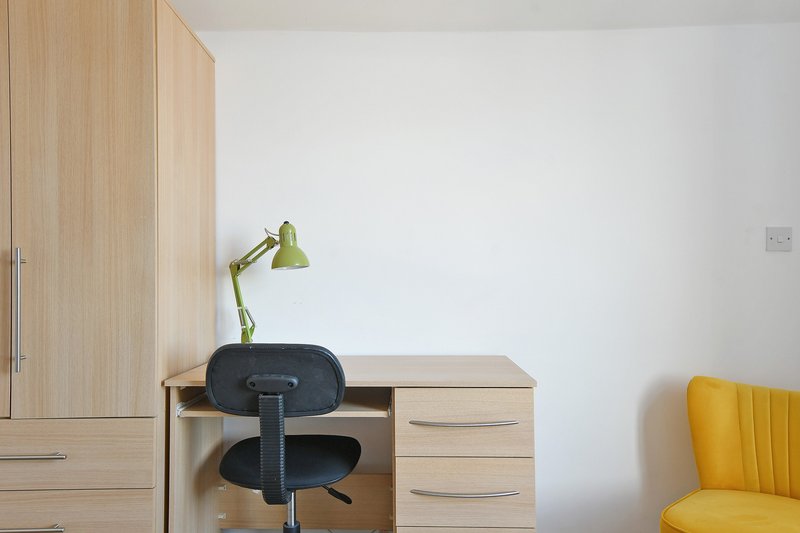 Bedroom desk with wooden drawers, black office chair, green desk lamp and yellow armchair