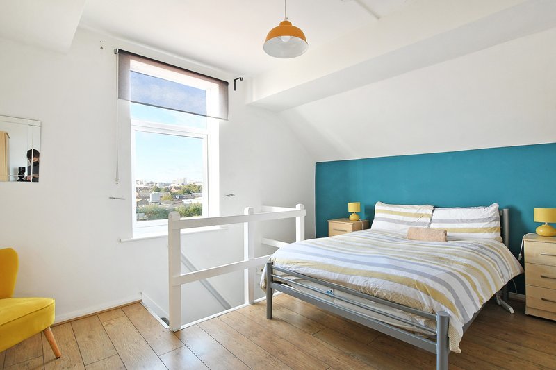 Bright bedroom with teal headboard, double bed, wooden floor and window view