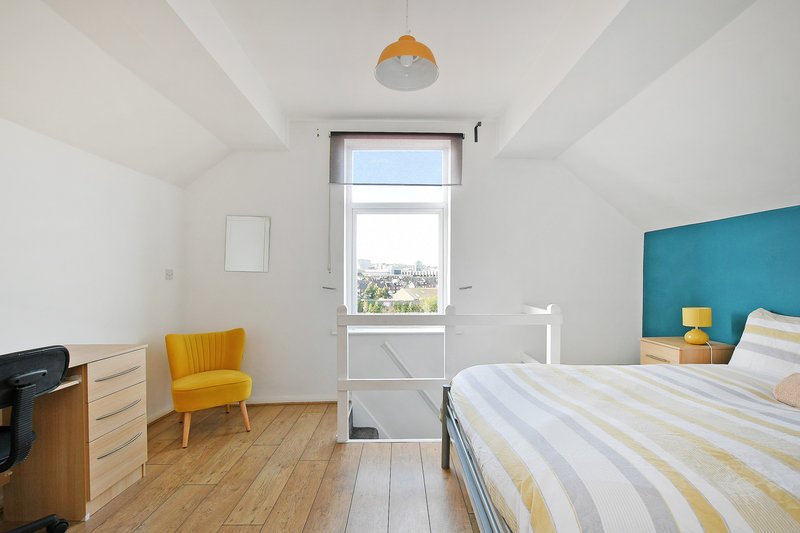 Bright bedroom with double bed, wooden floor, yellow chair and teal accent wall