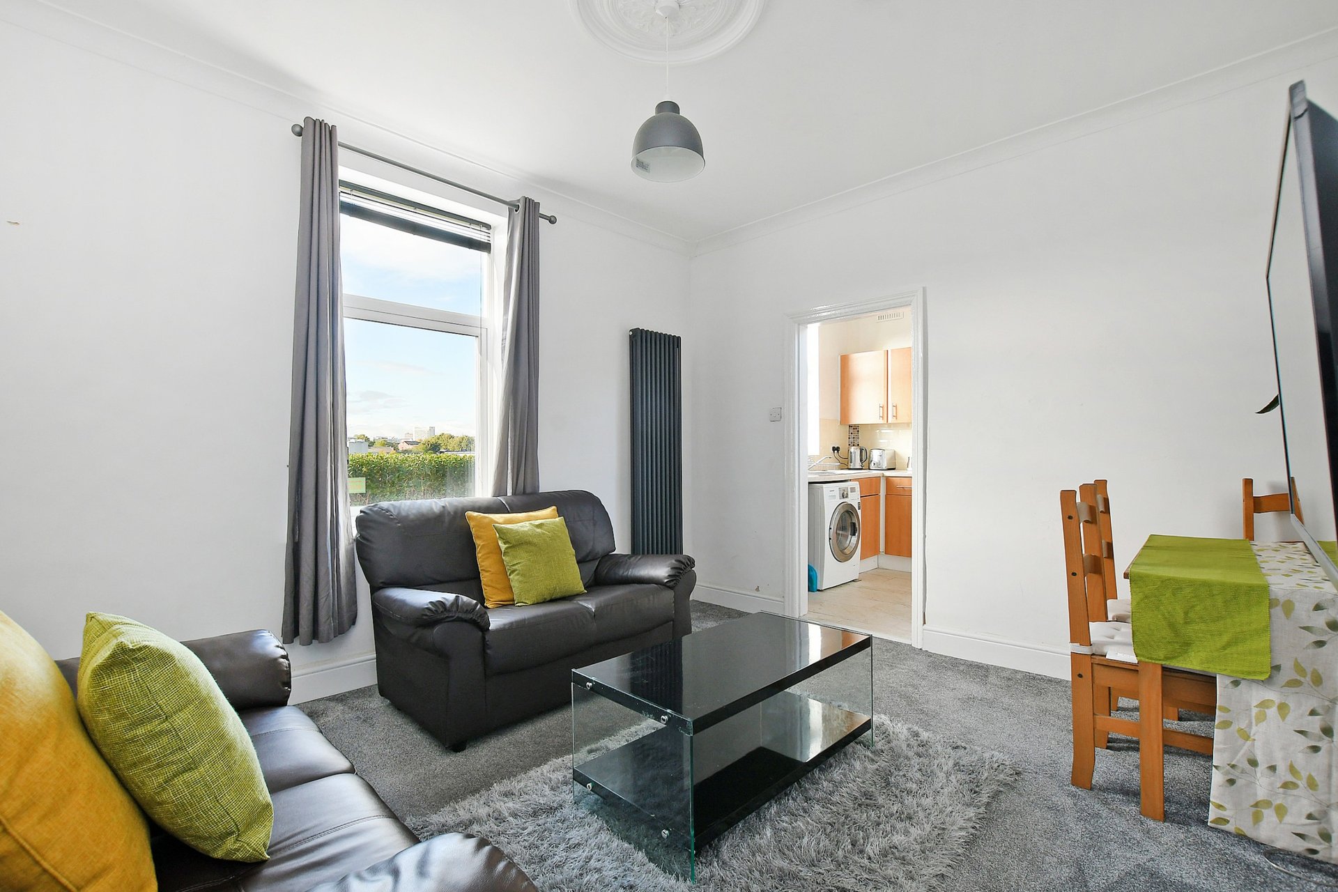 Bright living room with black leather sofa, glass coffee table, yellow cushions and window view