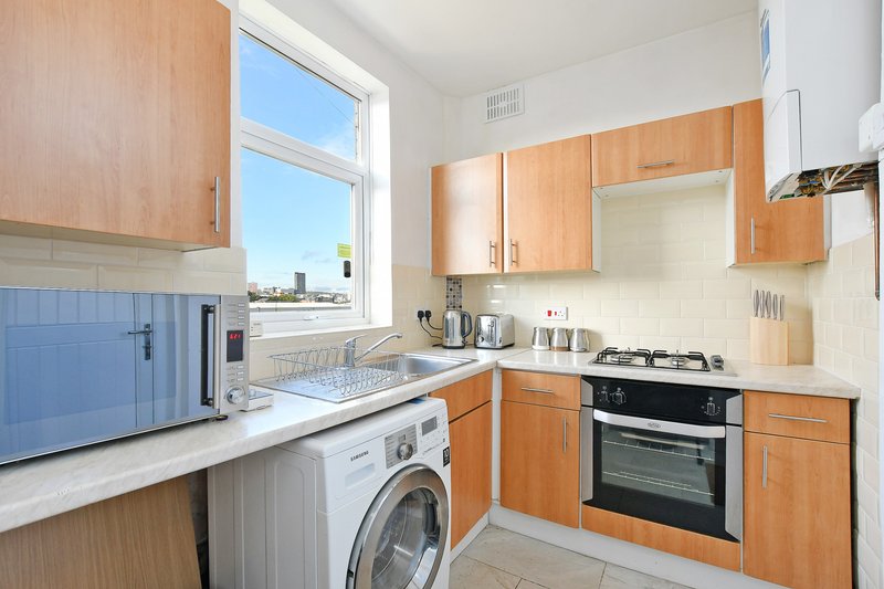 Kitchen with wooden cabinets, white countertops, washing machine, gas hob and oven