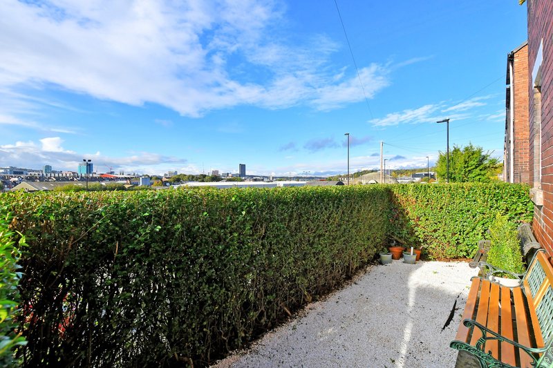 Outdoor patio area with orange bench, hedges and distant city skyline view