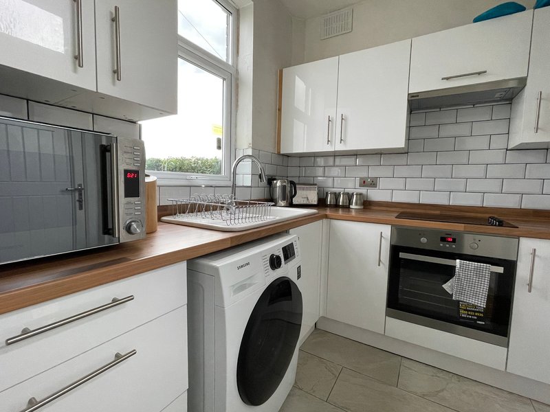 Modern kitchen with white cabinets, wooden countertops, integrated oven, washing machine and sink