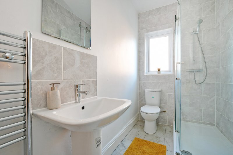 Modern bathroom with white pedestal sink, toilet, heated towel rail and glass shower enclosure