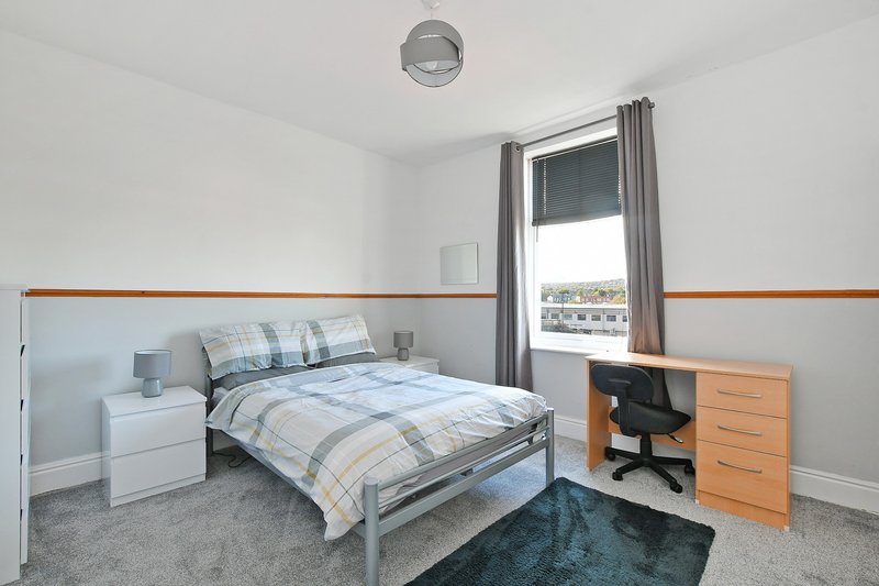 Bright bedroom with single bed, wooden desk, bedside table and window with city view