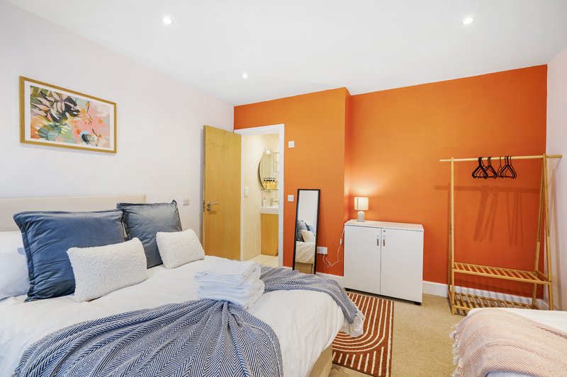 Bright bedroom with double bed, blue pillows, orange accent wall, wooden doors and clothing rail