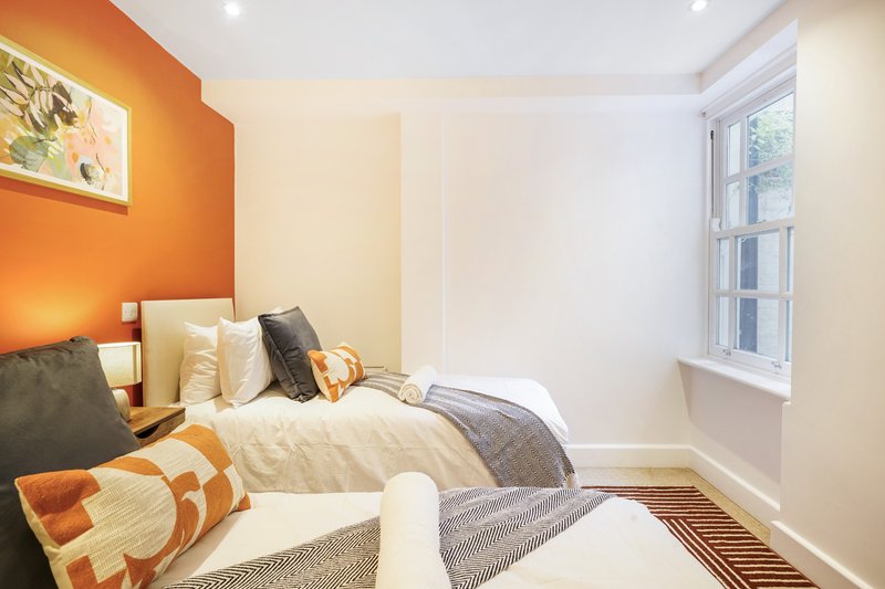 Bedroom with orange accent wall, double bed, cushions, and window with natural light