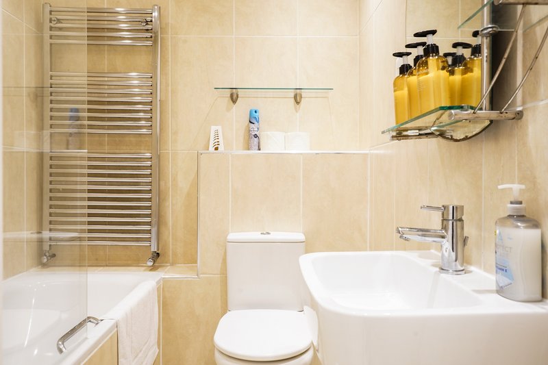 Modern bathroom with bathtub, toilet, sink, towel rail and toiletries shelf