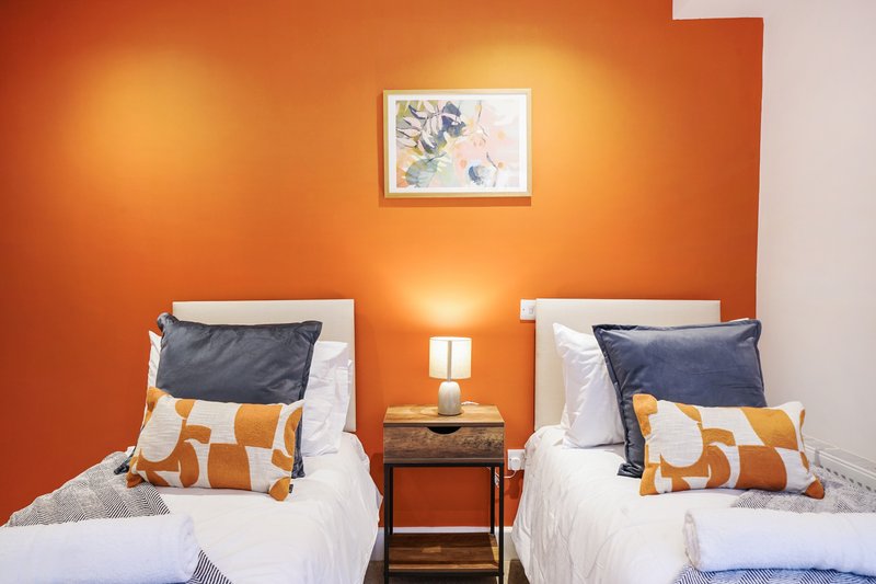 Twin bedroom with orange accent wall, two single beds, and framed floral artwork
