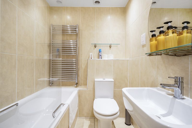 Bathroom with bathtub, toilet, sink, heated towel rail and yellow toiletries on shelf