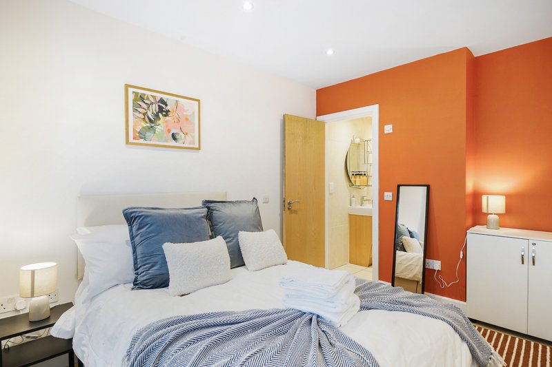Bedroom with double bed, blue and white bedding, orange accent wall, bedside lamps